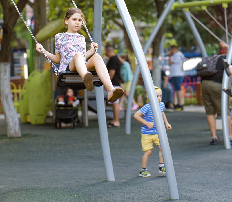 coming_soon_1 - A young child swinging on a modern playground swing set